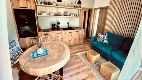 Obývací pokoj apartmánu: kulatý stůl z masivního dřeva, petrolejová rozkládací pohovka, kuchyňská linka a stěna z dřevěných lamel
