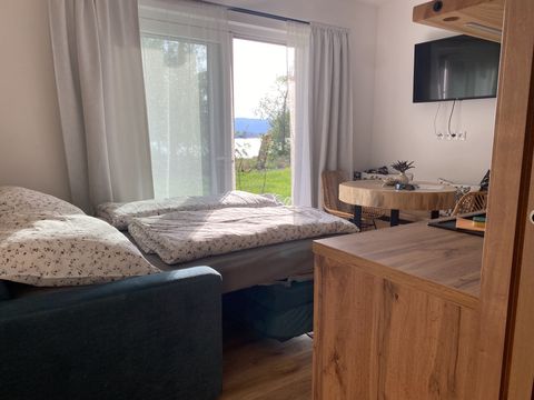 Roh obýváku s televizí na stěně, oknem do zahrady a rozloženou pohovkou ustlanou pro dva
