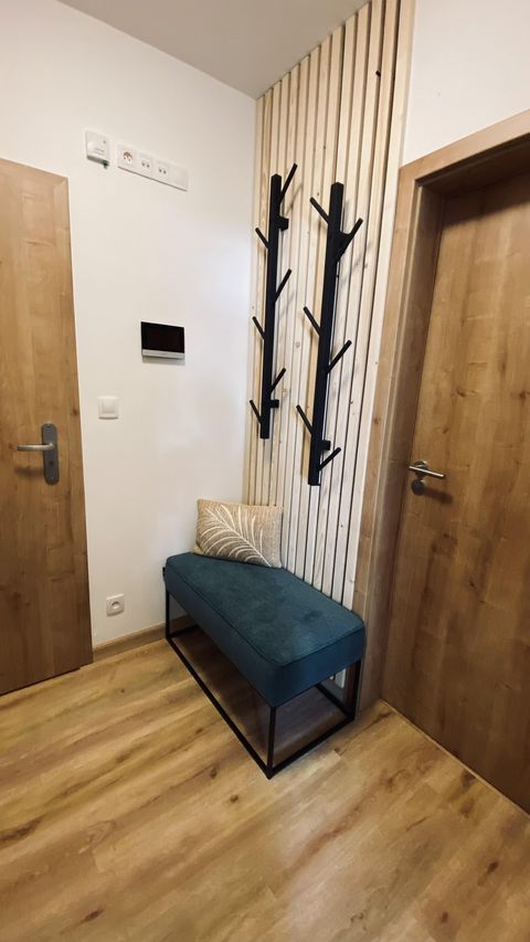 Zádveří apartmánu s věšáky ve tvaru větví, čalouněnou lavicí, dřevěnými dveřmi a stěnou z lamel